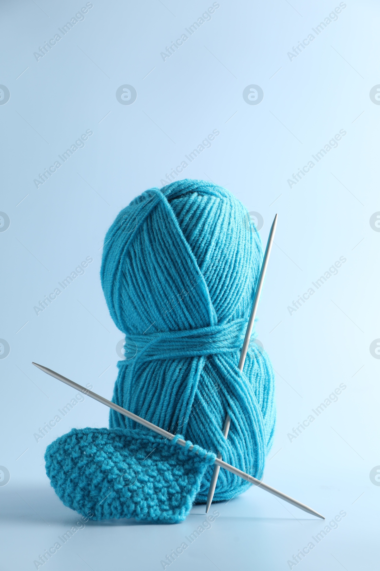 Photo of Skein of yarn, knitting needles and pattern sample on light background