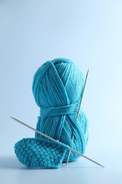 Photo of Skein of yarn, knitting needles and pattern sample on light background