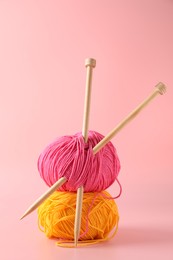 Colorful yarns and knitting needles on pink background