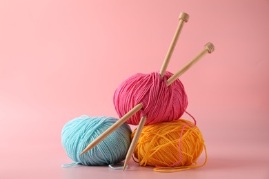 Colorful yarns and knitting needles on pink background