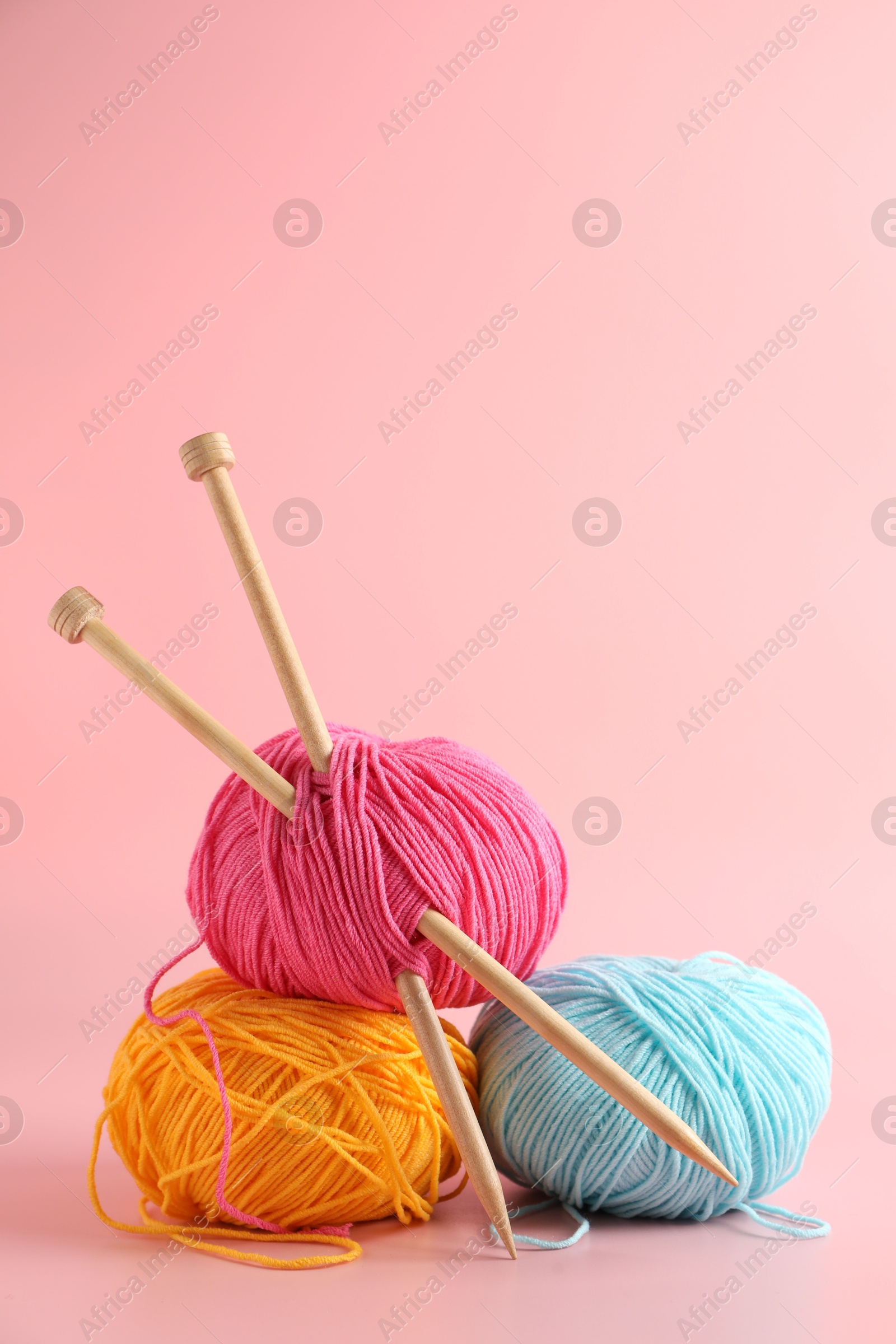 Photo of Colorful yarns and knitting needles on pink background. Space for text