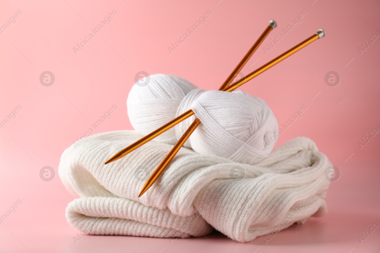 Photo of Skein of yarn with knitting needles and sweater on pink background, closeup