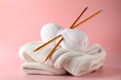 Skein of yarn with knitting needles and sweater on pink background, closeup