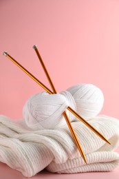 Photo of Skein of yarn with knitting needles and sweater on pink background, closeup