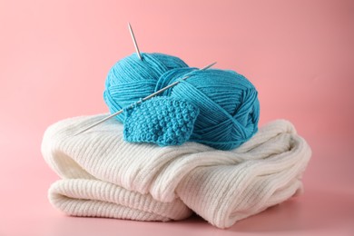 Skein of yarn with knitting needles, pattern sample and sweater on pink background, closeup