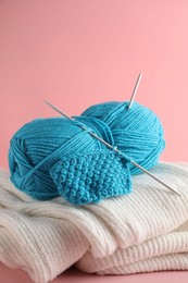 Photo of Skein of yarn with knitting needles, pattern sample and sweater on pink background, closeup