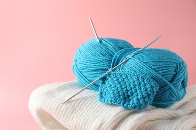 Photo of Skein of yarn with knitting needles, pattern sample and sweater on pink background, closeup