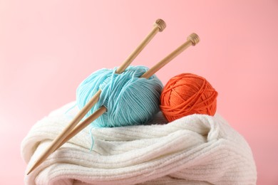 Different yarns, knitting needles and sweater on pink background, closeup