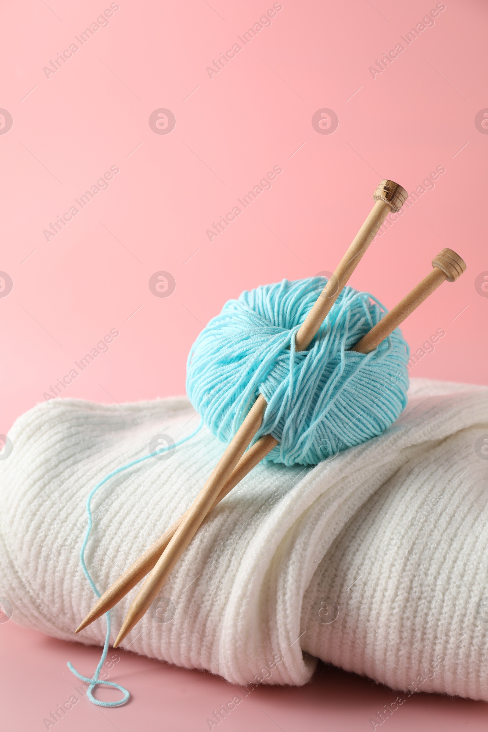 Photo of Ball of yarn with knitting needles and sweater on pink background