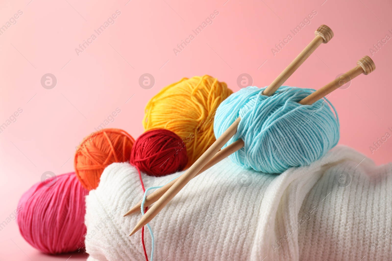 Photo of Different yarns, knitting needles and sweater on pink background, closeup