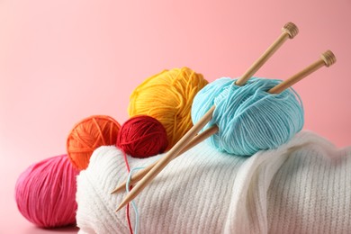 Different yarns, knitting needles and sweater on pink background, closeup