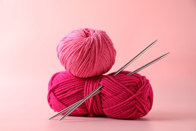 Different yarns and knitting needles on pink background, closeup