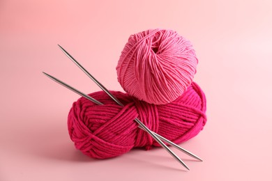 Different yarns and knitting needles on pink background, closeup