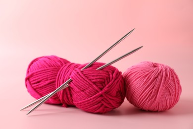 Different yarns and knitting needles on pink background, closeup