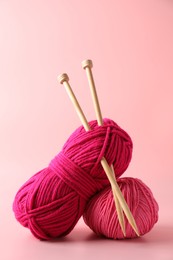 Different yarns and knitting needles on pink background