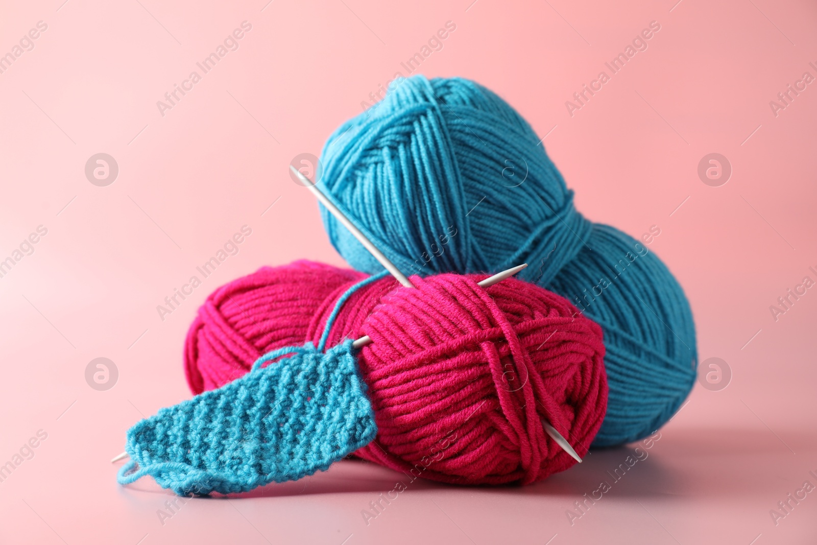 Photo of Different yarns, knitting needles and pattern sample on pink background, closeup