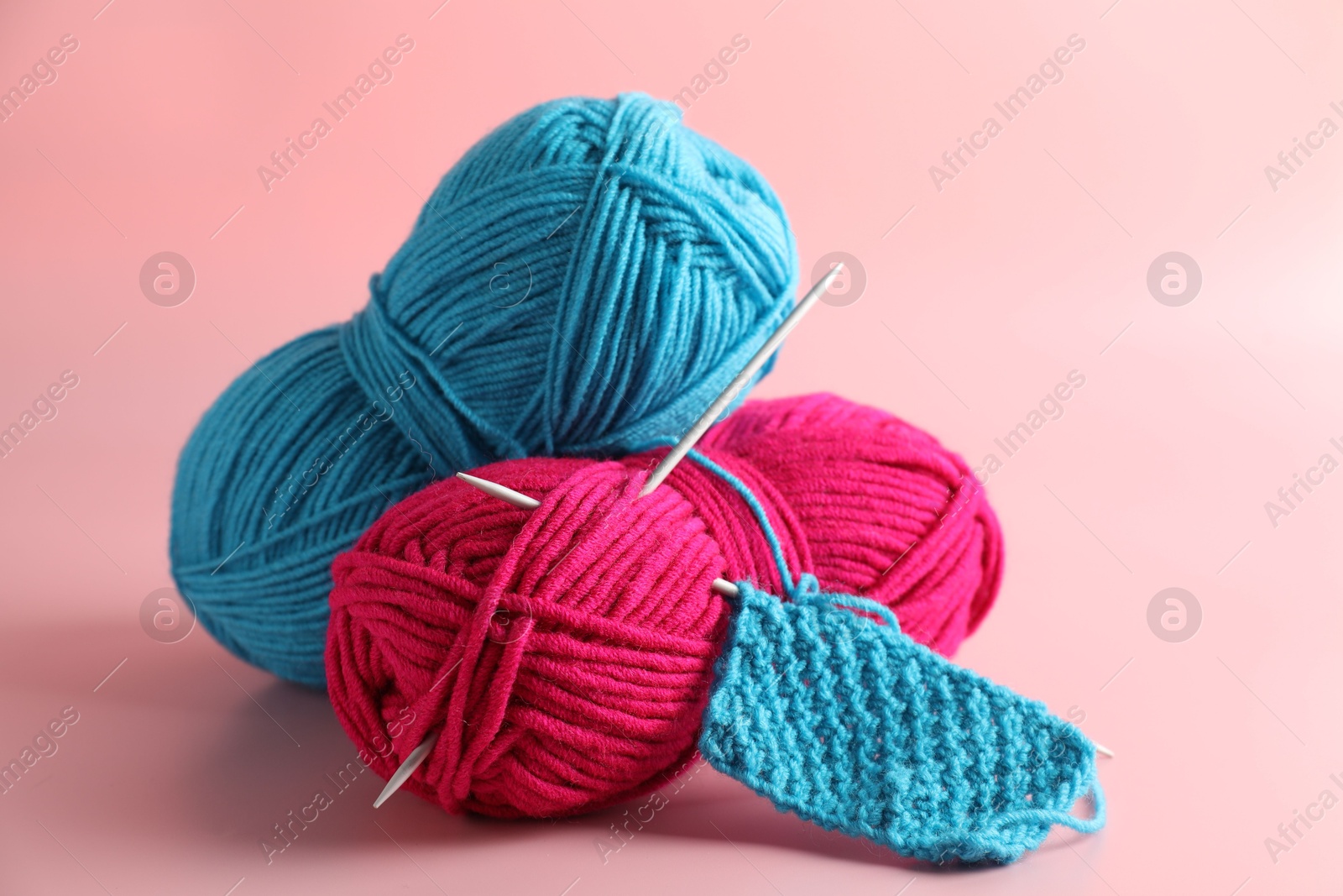 Photo of Different yarns, knitting needles and pattern sample on pink background, closeup