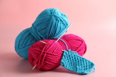 Different yarns, knitting needles and pattern sample on pink background, closeup