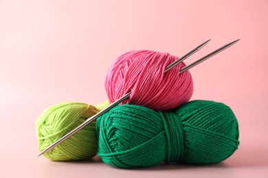 Different yarns and knitting needles on pink background, closeup