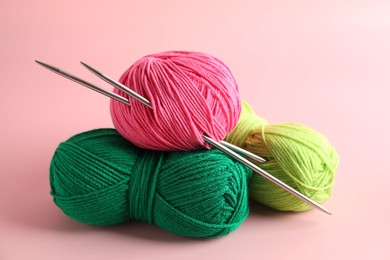 Different yarns and knitting needles on pink background, closeup