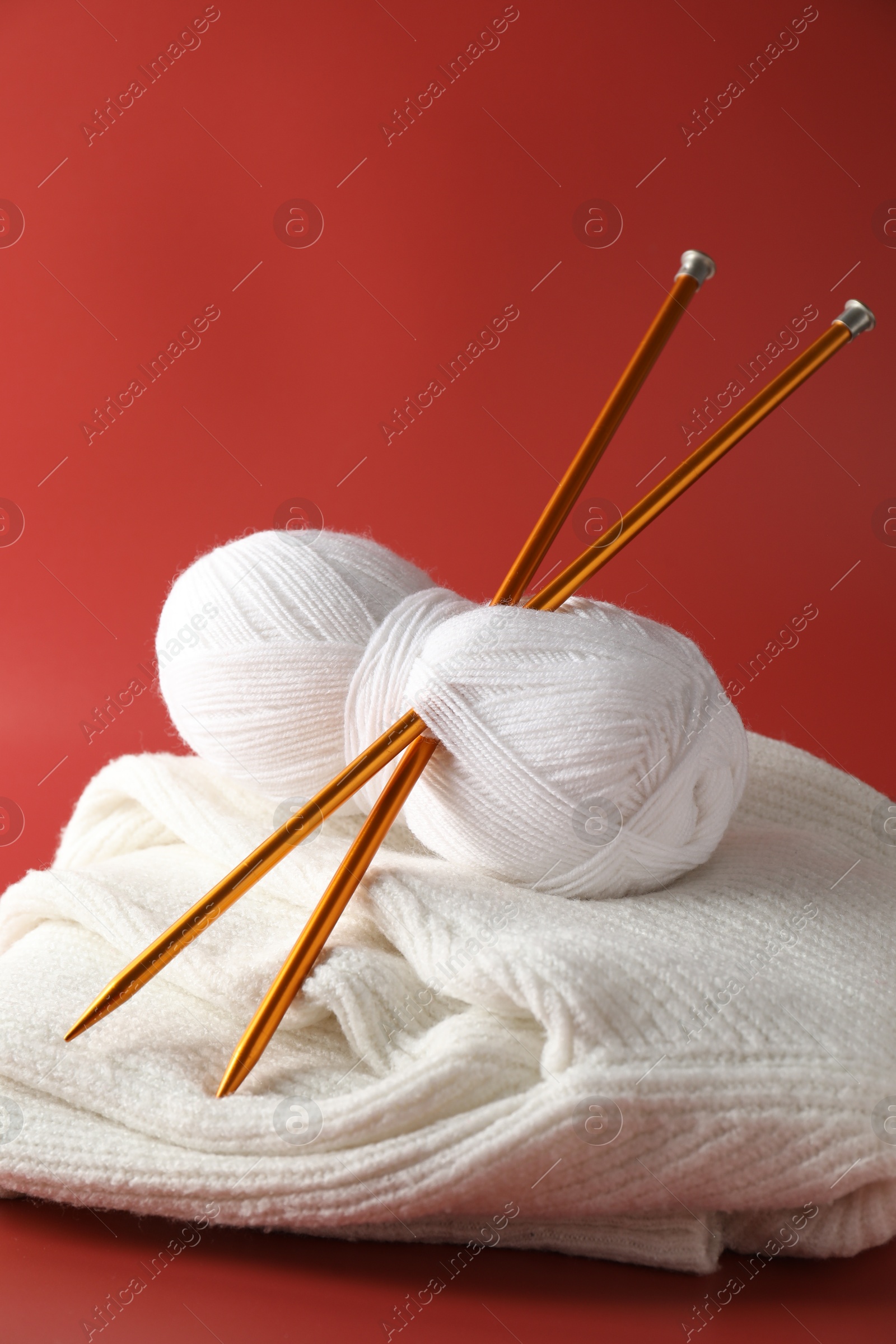 Photo of Skein of yarn with knitting needles and sweater on red background