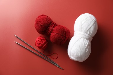 Different colorful yarns and knitting needles on red background, flat lay