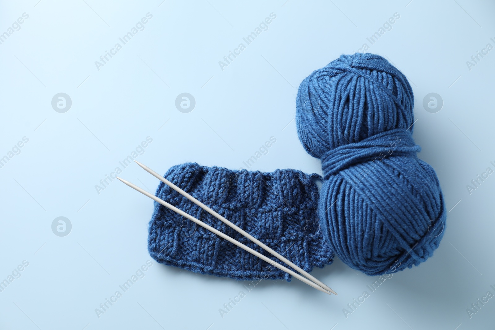 Photo of Skein of yarn, knitting needles and pattern sample on light blue background, flat lay. Space for text