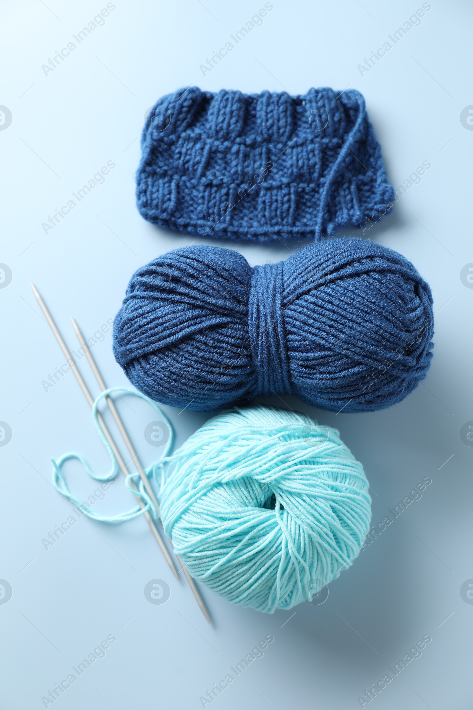 Photo of Bright yarns, knitting needles and pattern sample on light blue background, flat lay