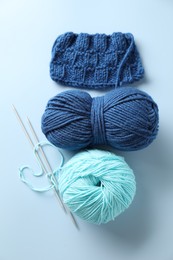 Photo of Bright yarns, knitting needles and pattern sample on light blue background, flat lay