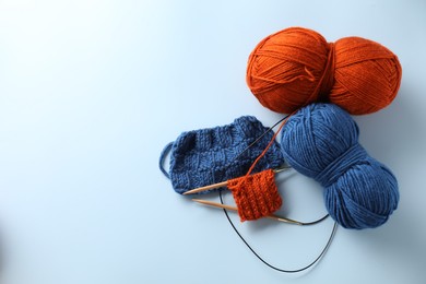 Bright yarns, knitting needles and pattern samples on light blue background, flat lay. Space for text