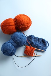 Photo of Bright yarns, knitting needles and pattern samples on light blue background, flat lay