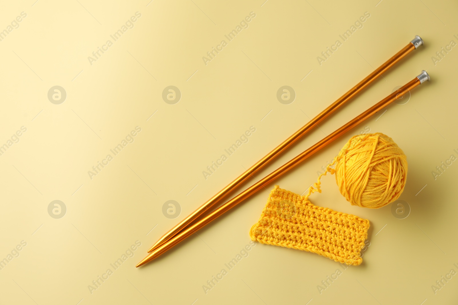 Photo of Ball of yarn, pattern sample and knitting needles on yellow background, flat lay. Space for text