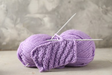 Skein of yarn, knitting needles and pattern sample on light textured table, closeup