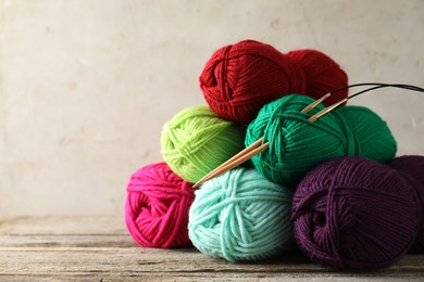 Photo of Pile of different yarns and knitting needles on wooden table, closeup. Space for text