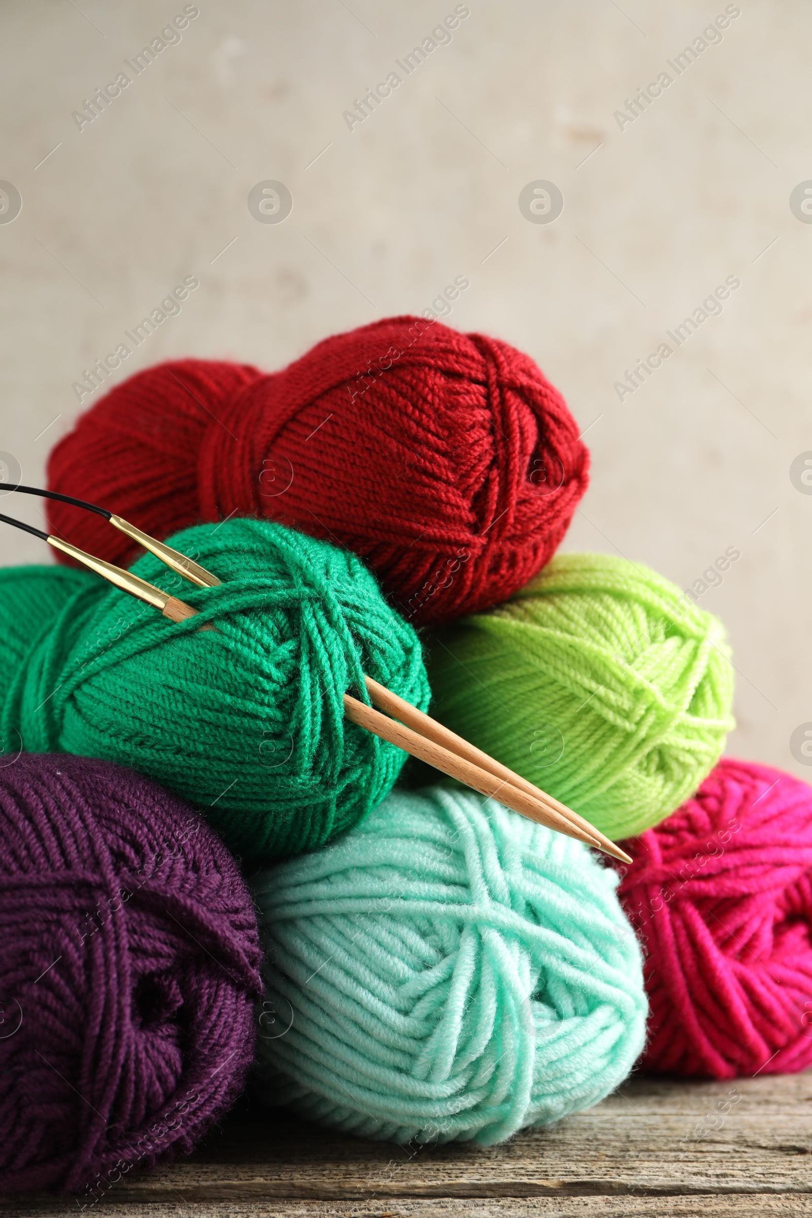 Photo of Pile of different yarns and knitting needles on wooden table, closeup