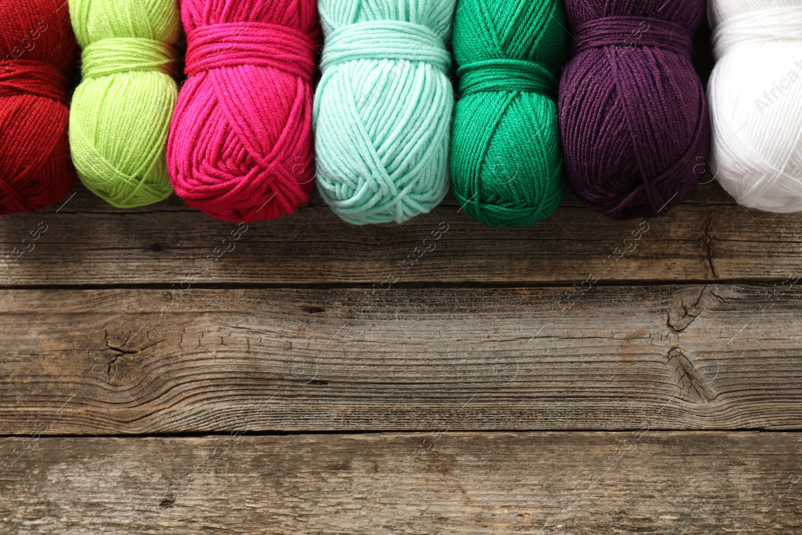 Photo of Different bright yarns on wooden table, flat lay. Space for text