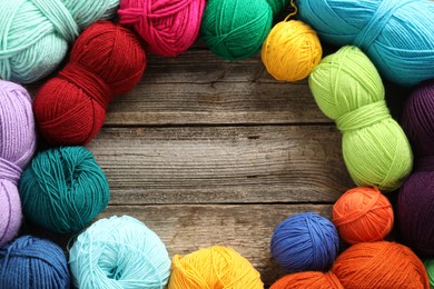 Frame of different bright yarns on wooden table, flat lay. Space for text