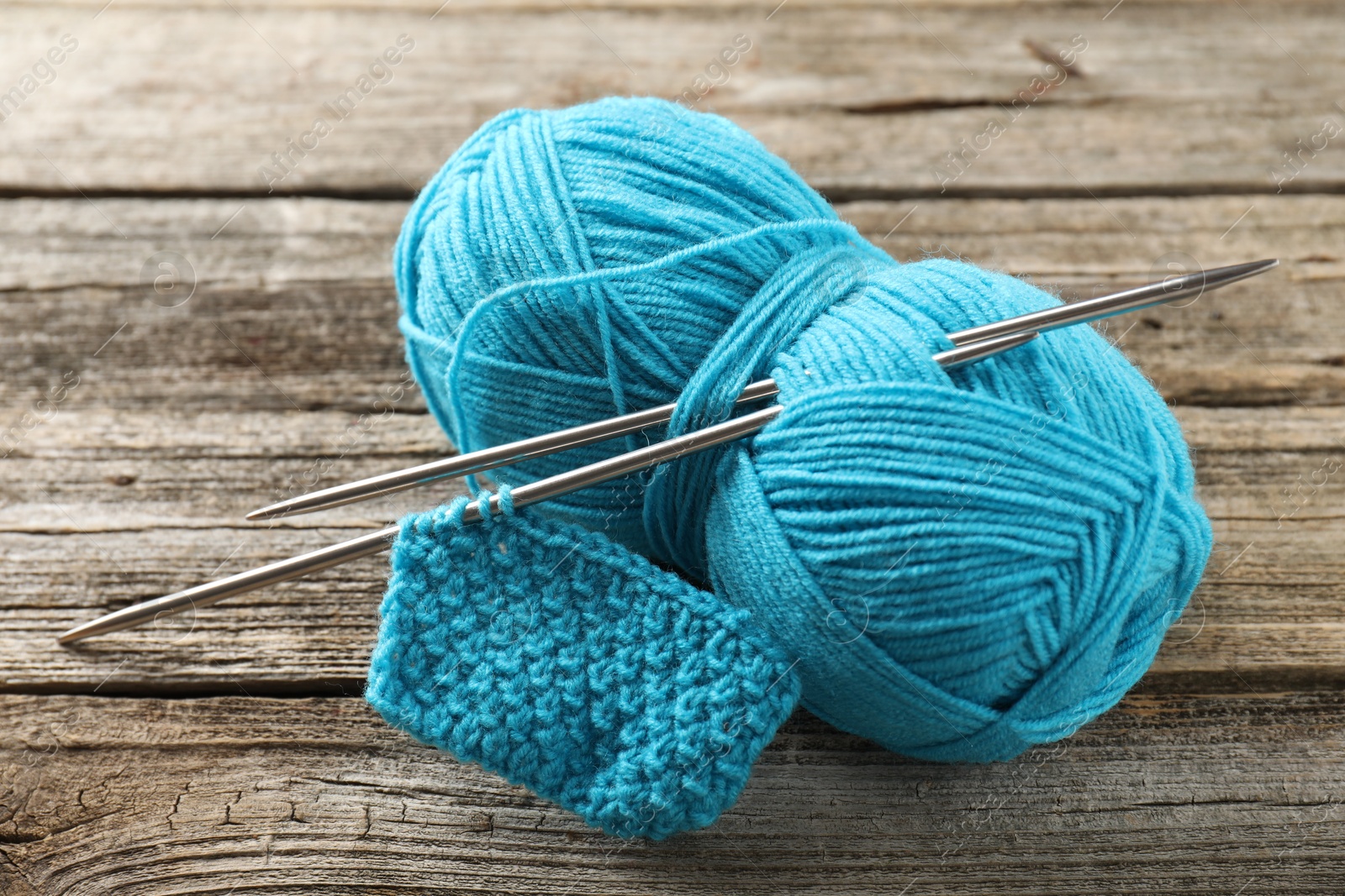 Photo of Skein of yarn, knitting needles and pattern sample on wooden table, closeup