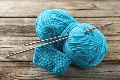 Photo of Skein of yarn, knitting needles and pattern sample on wooden table, closeup