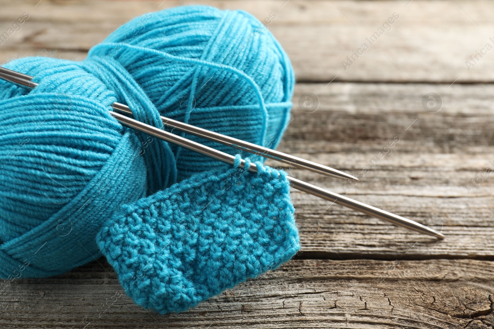 Photo of Skein of yarn, knitting needles and pattern sample on wooden table, closeup