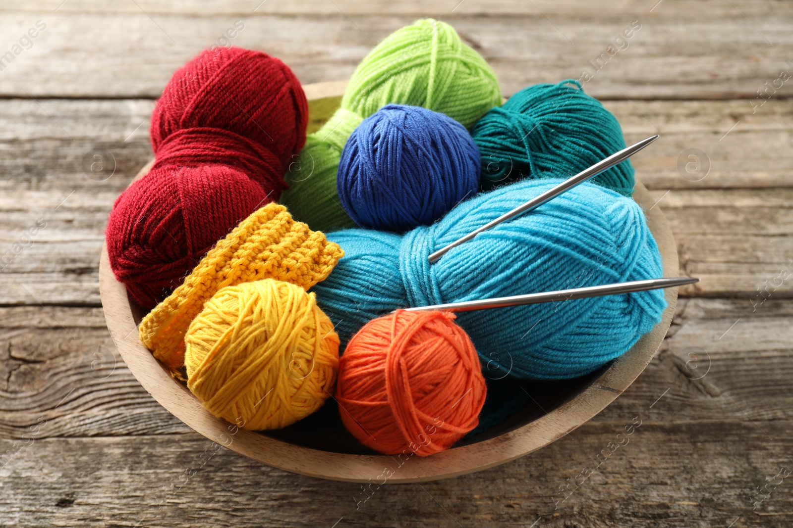 Photo of Different yarns, knitting needles and pattern sample in bowl on wooden table, closeup