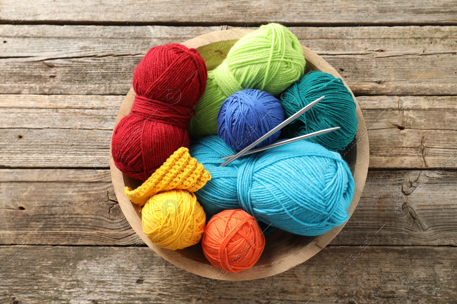 Photo of Different yarns, knitting needles and pattern sample in bowl on wooden table, top view