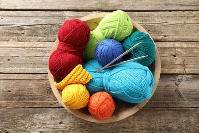 Photo of Different yarns, knitting needles and pattern sample in bowl on wooden table, top view