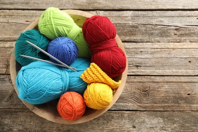 Different yarns, knitting needles and pattern sample in bowl on wooden table, top view. Space for text