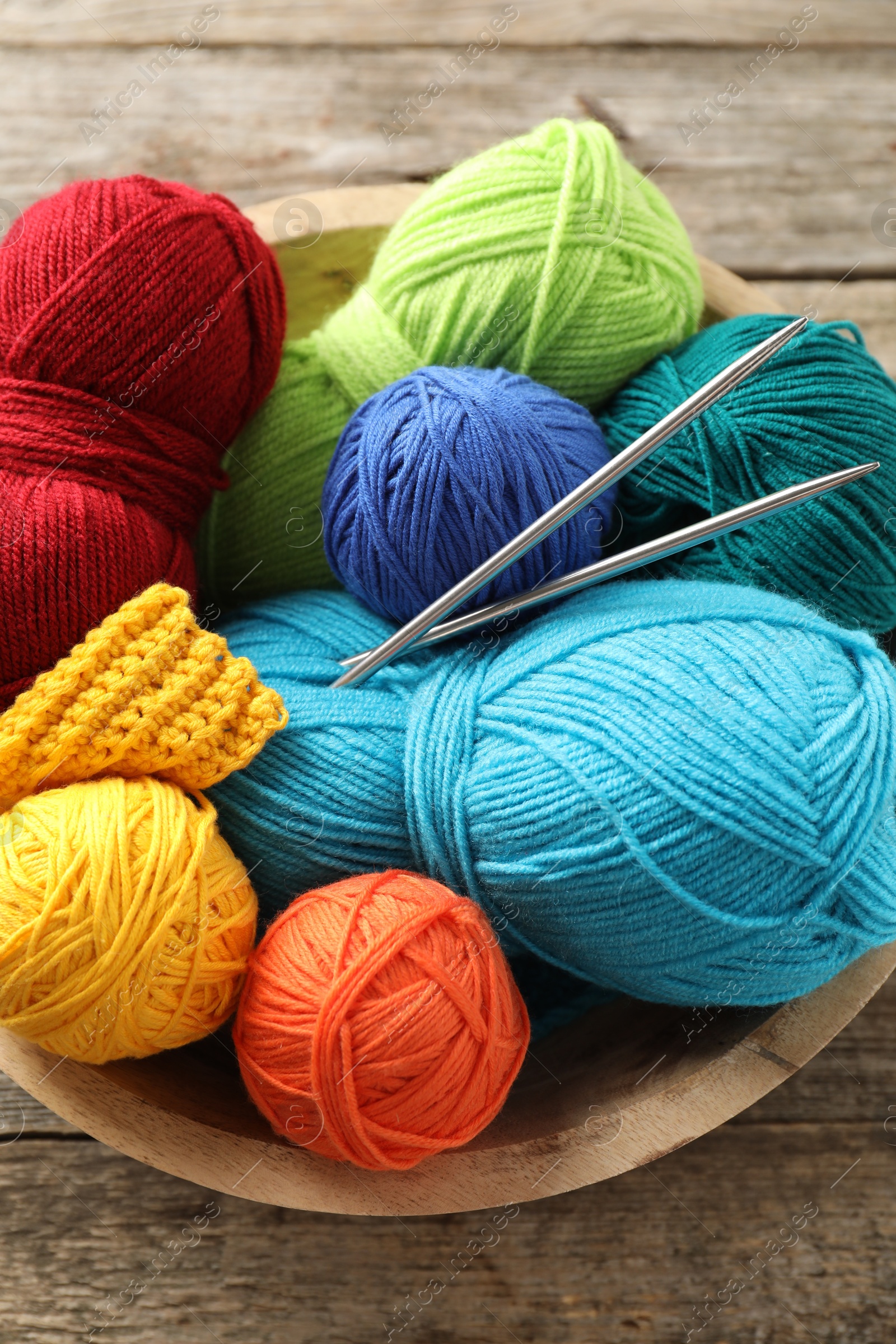 Photo of Different yarns, knitting needles and pattern sample in bowl on wooden table, above view