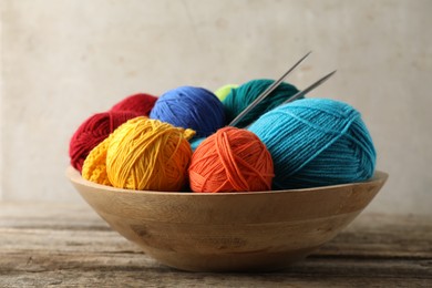 Different yarns, knitting needles and pattern sample in bowl on wooden table, closeup