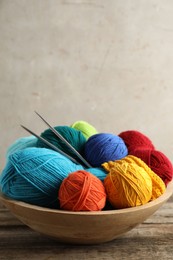 Different yarns, knitting needles and pattern sample in bowl on wooden table. Space for text