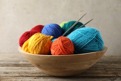 Different yarns, knitting needles and pattern sample in bowl on wooden table, closeup