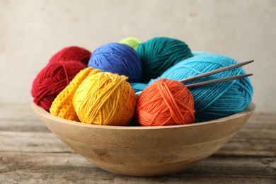 Different yarns, knitting needles and pattern sample in bowl on wooden table, closeup