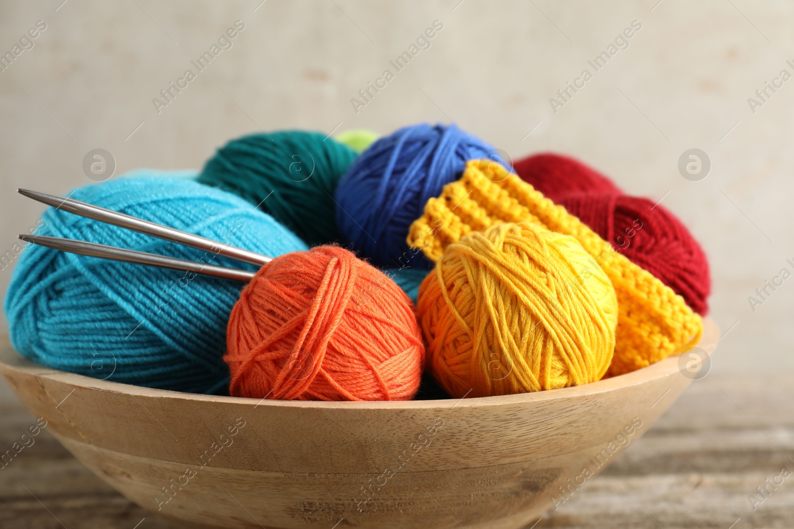 Photo of Different yarns, knitting needles and pattern sample in bowl on table, closeup